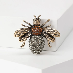 Vintage gold bee brooch featuring amber and grey rhinestones on a white display stand