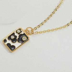 Macro view of gold plated necklace with black and white enamel flower pendant and small crystals