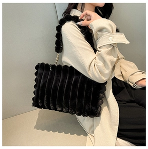 Detail of black faux fur tote bag with striped texture and decorative fur ball strap