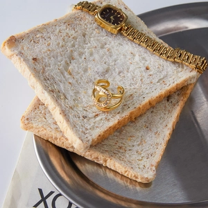 Gros plan d'une bague dorée avec strass et d'une montre carrée sur un support créatif