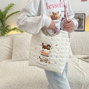 Detail of heart-quilted fabric and cute cat embroidery on a white tote bag with lilac handles