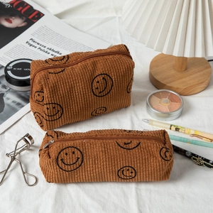 Brown corduroy cosmetic bag and brush case with smile face on white fabric background