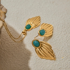 Close-up of golden shell-textured necklace and turquoise earrings on stone