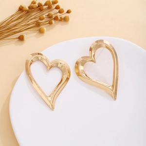 Macro detail of golden hollow heart earrings on white stand with dry flower accents