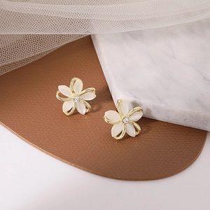 Detailed view of flower earrings with ivory petals, gold trim and sparkling rhinestone center
