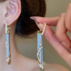 Detail shot of heart pearl earrings with long blue and white tassel chains on model