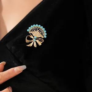 Vintage gold fan-shaped brooch with blue beads and rhinestone bow on black fabric