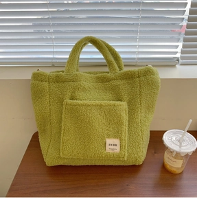 Green faux shearling tote bag with front pocket on a wooden surface in natural light