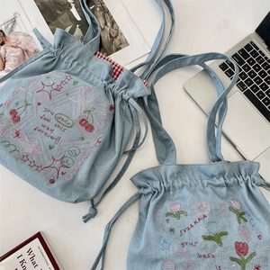 Detailed view of light blue denim tote bags with floral embroidery and red checkered lining