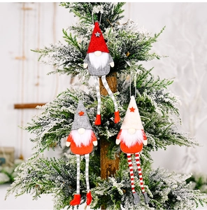 Three plush Christmas gnomes with long legs hanging on a snowy festive tree branch