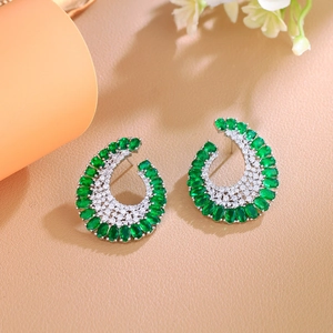 Macro detail of C-shaped earrings with emerald green stones and pavé cubic zirconia