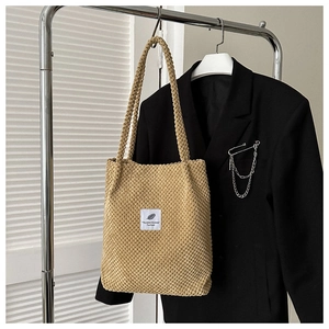 Detail of light brown popcorn texture tote bag with white tag on a black suit jacket