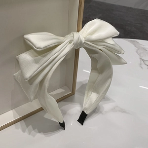 Close-up of a white satin triple-layered bow headband on a marble surface background