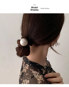 Dettaglio dell'elastico con grande perla crema su uno chignon basso di modella
