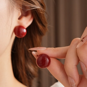 Primo piano di un modello che indossa un orecchino a bottone tondo rosso scuro lucido