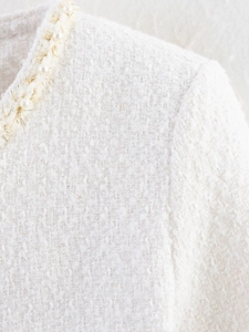 Gros plan sur une veste en tweed blanc avec perles élégantes et bordures dorées en lurex