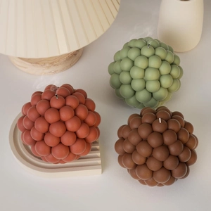 Detailed view of bubble ball scented candles in rust red, moss green and dark brown colors
