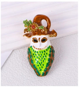 Detail of owl brooch with brown hat and green enamel body on white textured background
