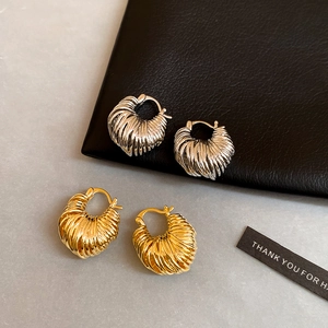 Macro shot of gold and silver plated twisted U-shaped hoop earrings on elegant marble and leather