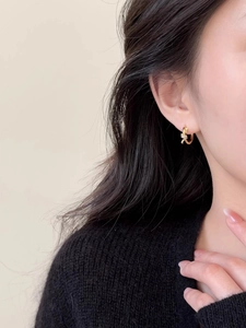 Détail de boucles d'oreilles nœud dorées avec zircons portées par un mannequin de profil