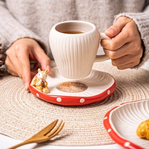 Detail of red mushroom ceramic saucer and beige striped teacup on a woven mat