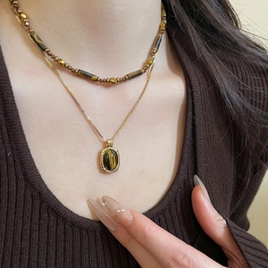 Close-up of double-layer necklace with tiger eye beads and gold pendant on a model