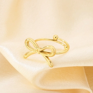Elegant gold bow-shaped stainless steel adjustable ring displayed on champagne silk fabric