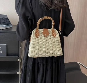 Detail of woven straw bag with bamboo handle and brown leather flap on a model