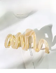 Detail shot of a wavy acetate hair claw clip with beige and gold marble texture finish