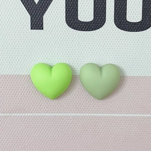Flat lay detail of macaron heart-shaped resin accessories in green on canvas texture