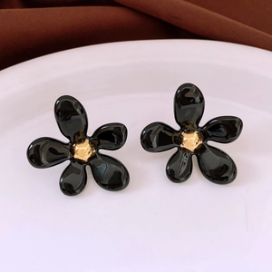 Détail de boucles d'oreilles fleurs noires et pistils dorés sur une assiette blanche