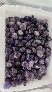 Macro shot of 15mm polished heart-shaped amethyst gemstones in a white tray