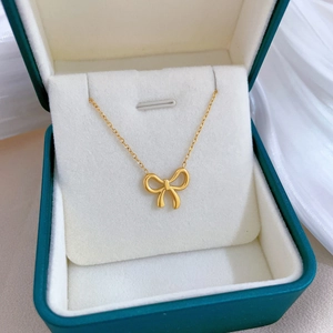 Close-up of golden bow pendant necklace resting in a premium green jewelry gift box