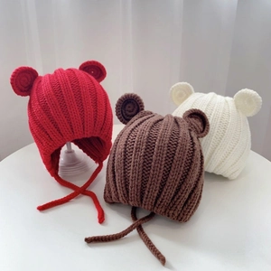 Three knit baby beanies with bear ears in red, brown, and white on a white table