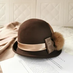 Close-up of wool cloche hat in dark brown with champagne ribbon and fluffy fur pom-pom