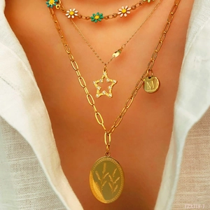 Detail of multi-layer gold necklace set featuring daisy beads and M letter pendant