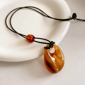 Detail shot of amber-colored resin teardrop pendant with black woven cord and red bead