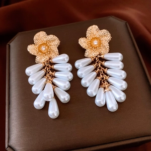 Detail view of gold flower earrings with teardrop pearl tassels and sparkling zircon center