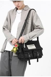 Detail of black canvas messenger bag featuring multiple pockets and green dinosaur charm