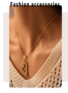 Detail of a large hollow heart pendant on a gold bead chain worn by a model
