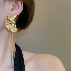 Detail view of long gold metallic flower earrings with cascading tassels on a model