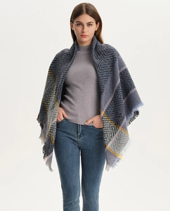Detail of knit plaid shawl featuring blue, grey and yellow geometric patterns with fringes