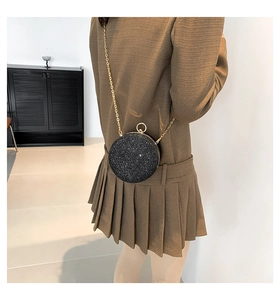 Sac bandoulière rond noir pailleté avec chaîne dorée porté par un mannequin