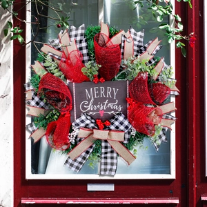 Christmas wreath with red ribbons, plaid bows, and Merry Christmas sign on a red wooden door