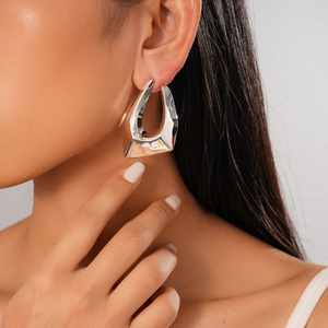 Macro view of a large irregular geometric silver-tone earring worn on a model's ear