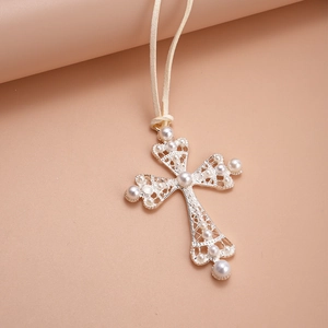 Macro shot of silver cross pendant with faux pearl inlays on beige suede cord