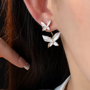 Détail des boucles d'oreilles double papillon en émail blanc perle et métal doré sur modèle