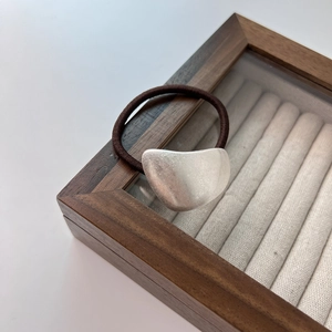 Minimalist elastic hair tie with silver matte geometric metal charm on a wooden box