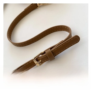 Detail of a brown leather adjustable shoulder strap with a golden metal buckle and stitching