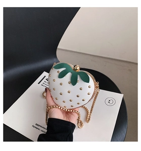 Detailed close-up of a strawberry-shaped mini bag with gold studs and a metallic chain